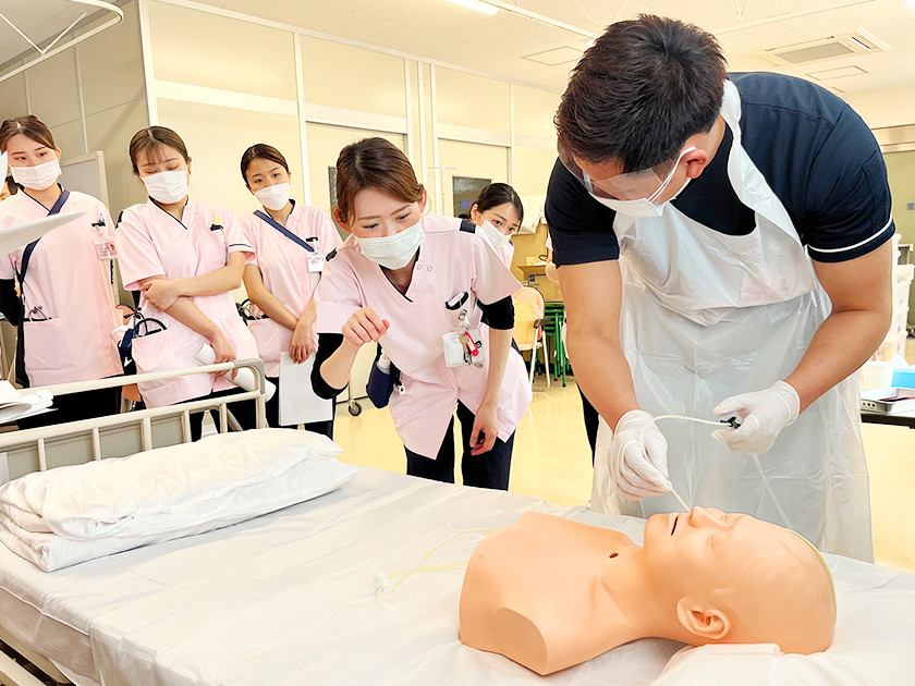 写真：人物模型をベッドに横たえて、作業について説明を受けている様子