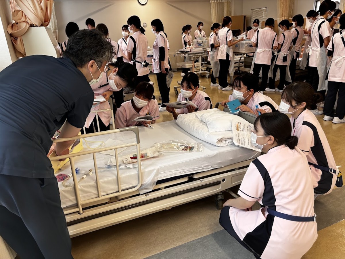 写真：人物模型をベッドに横たえて、作業について説明を受けている様子